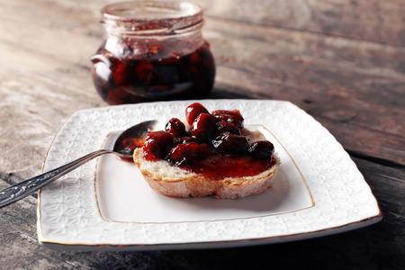 Fresh bread with jam on plate on wooden background