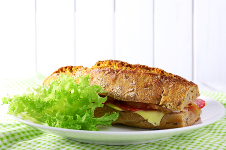Fresh and tasty sandwich with ham and lettuce on plate on wooden backgroundの写真素材