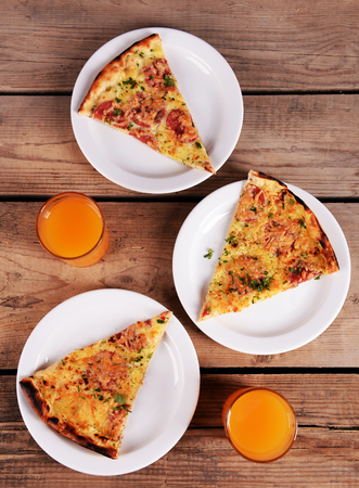 Tasty slices of pizza on plates with glasses of juice on wooden tableの写真素材