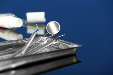 Dentist tools in metal tray with toothpaste and brush on blue backgroundの写真素材