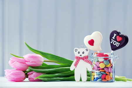 Beautiful pink tulips with jar of sweets  on table on light backgroundの写真素材