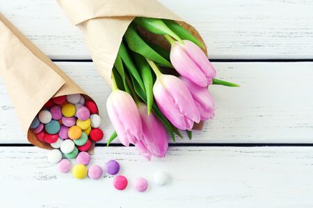 Beautiful pink tulips in paper with sweets on wooden background