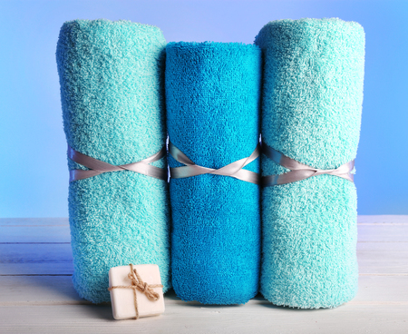 Rolled tied towels with soap on wooden table and light colorful backgroundの写真素材