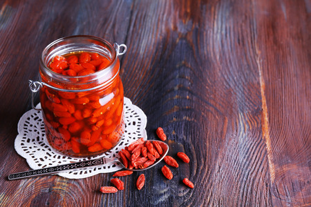 Goji berries in glass bottle on lace doily with silver spoon on rustic wooden table backgroundの写真素材