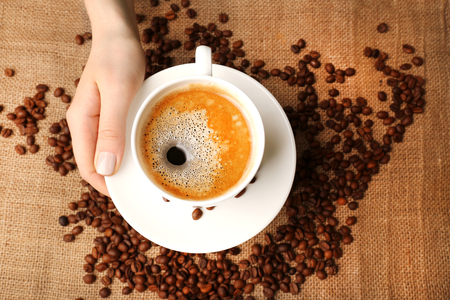Female hand holding cup with coffee beans on burlap cloth, top viewの写真素材