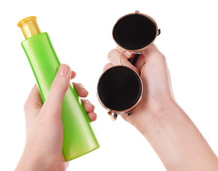 Bottle of suntan cream and sunglasses in female hands isolated on whiteの写真素材