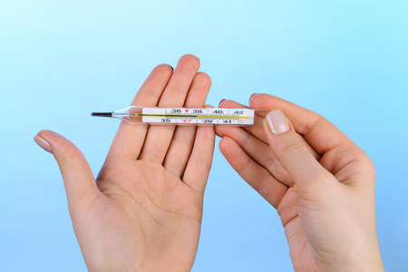 Female hands holding thermometer on blue background