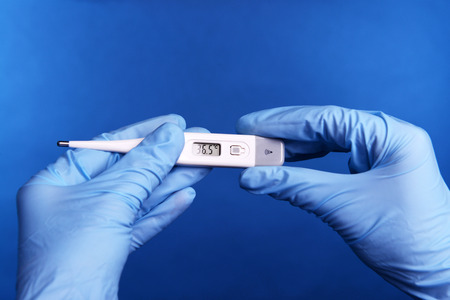 Hands with gloves holding thermometer on blue backgroundの写真素材