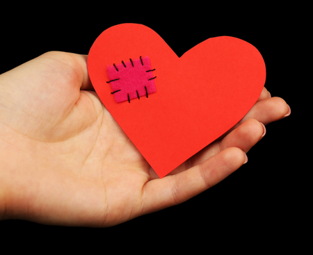 Female hand holding broken heart with patch on black background