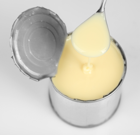 Tin can of condensed milk with spoon isolated on whiteの写真素材