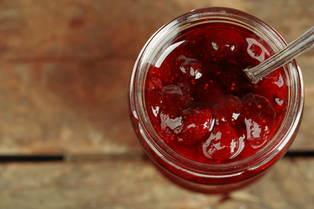 Jar of strawberry jam with spoon on wooden background
