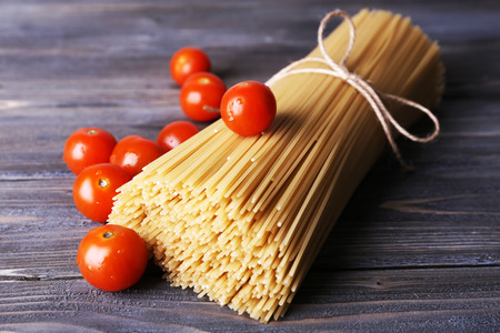 Raw pasta and tomatoes on wooden backgroundの写真素材