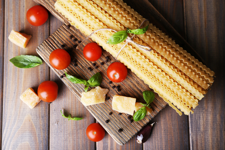Raw pasta with cheese and vegetables on wooden backgroundの写真素材