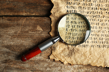 Grunge paper with hieroglyphics with magnifier on wooden backgroundの写真素材