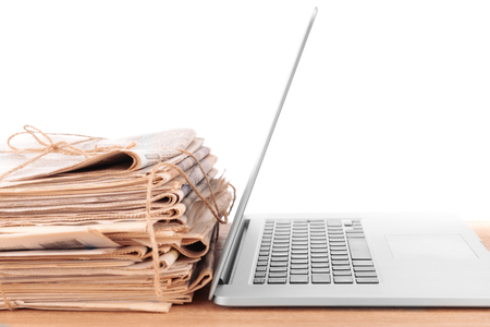 Laptop with stack of newspapers on table isolated on whiteの写真素材