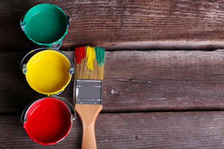 Metal buckets with colorful paint near brush on wooden backgroundの写真素材