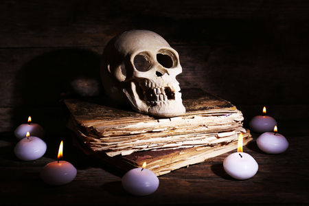 Still life with human skull, retro book and candlelight in dark on wooden table, closeupの写真素材