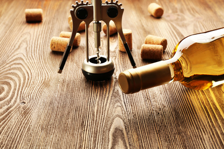 Glass bottle of wine with corks and corkscrew on wooden table background
