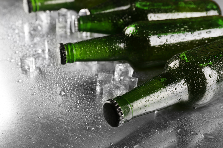 Glass bottles of beer with ice cubes on wet table backgroundの写真素材