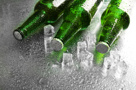 Glass bottles of beer with ice cubes on wet table backgroundの写真素材