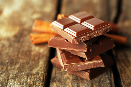 Pieces of chocolate with cinnamon sticks on wooden backgroundの写真素材