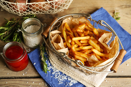 Tasty french fries and fresh potatoes in metal baskets on wooden table background