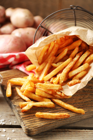 Tasty french fries on cutting board, on wooden table backgroundの写真素材
