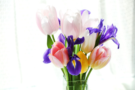 Beautiful bouquet of spring flowers in glass vase on curtain backgroundの写真素材