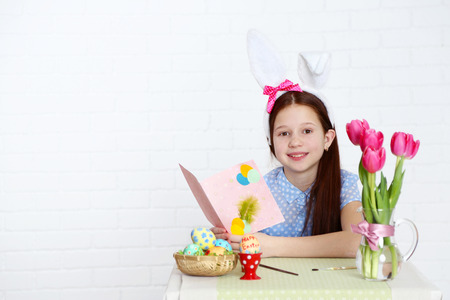 Cute girl with greeting card and decorated Easter eggs, on light backgroundの写真素材