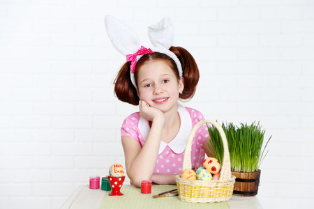 Cute girl decorates Easter eggs, on light background