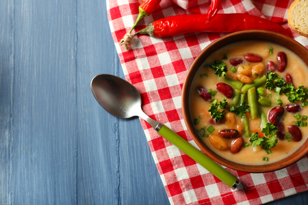 Bean soup in bowl with fresh sliced bread on napkin, on color wooden table backgroundの写真素材