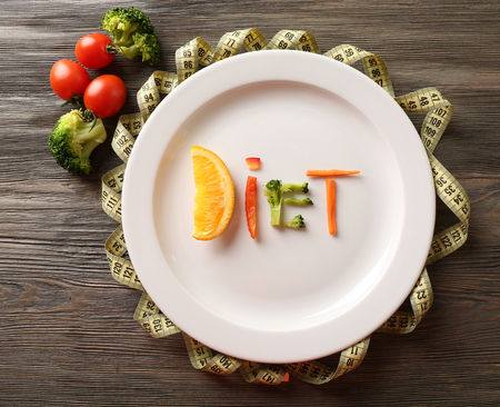 Word DIET made of sliced vegetables in plate with measuring tape on wooden table, top viewの写真素材