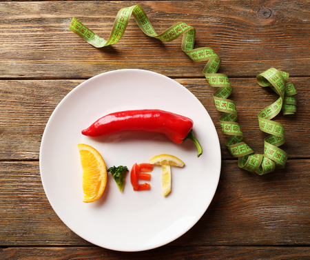 Word DIET made of sliced vegetables in white plate with measuring tape on wooden table, top viewの写真素材