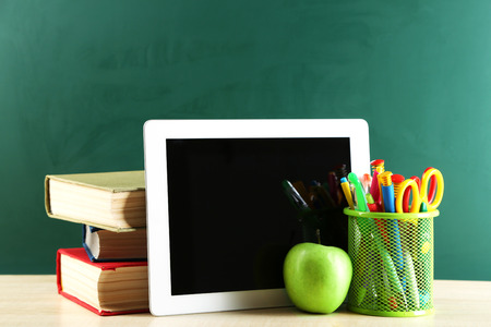 Digital tablet, books, colorful pens and apple on desk in front of blackboardの写真素材