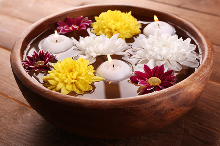 Bowl of spa water with flowers and candles on wooden table, closeupの写真素材