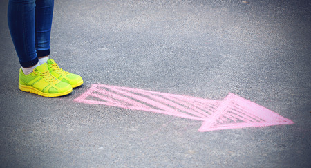 Female feet and drawing arrow on pavement background