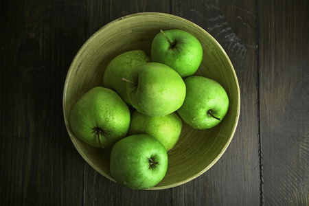 Green apples in bowl on wooden table, top viewの写真素材