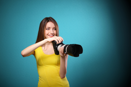 Young female photographer taking photos on blue backgroundの写真素材