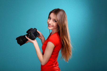 Young female photographer taking photos on blue background
