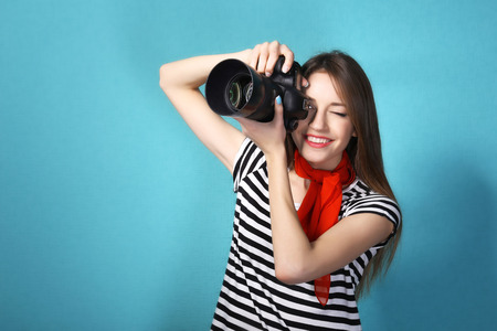 Young female photographer taking photos on blue backgroundの写真素材