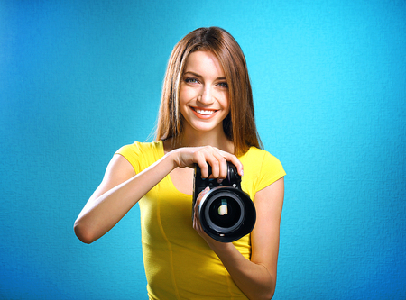 Young female photographer taking photos on blue background