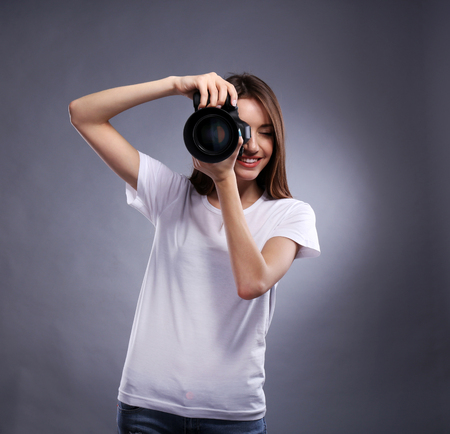 Young female photographer taking photos on grey background