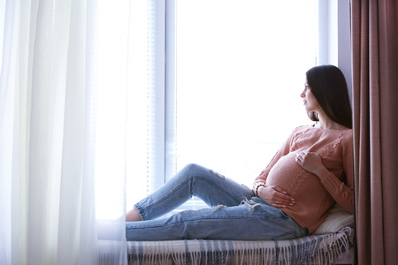 Pregnant woman sitting on windowsill backgroundの写真素材