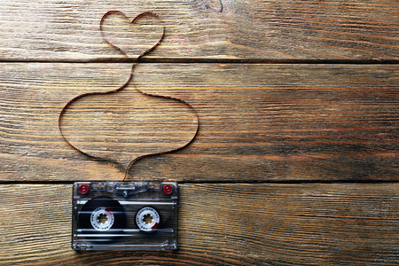 Audio cassette with magnetic tape in shape of heart on wooden backgroundの写真素材