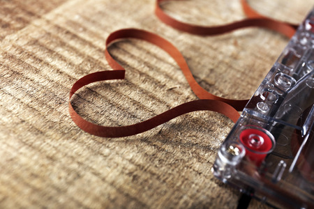 Audio cassette with magnetic tape in shape of hearts on wooden background