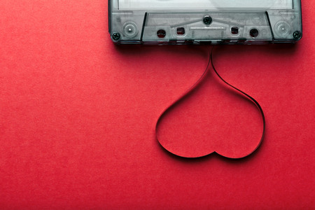 Audio cassette with magnetic tape in shape of heart on red background
