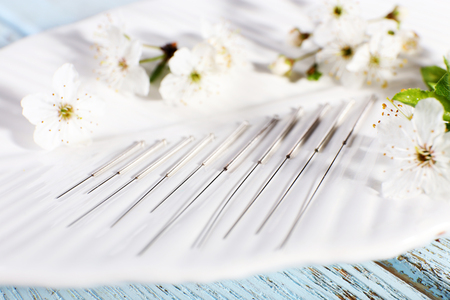 Acupuncture needles and flowering branch on plate on wooden table, closeupの写真素材