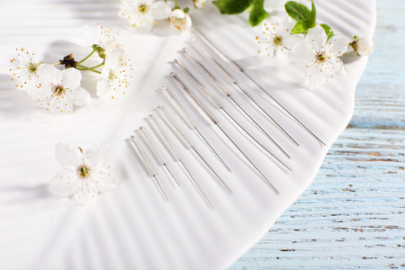 Acupuncture needles and flowering branch on plate on wooden table, closeupの写真素材