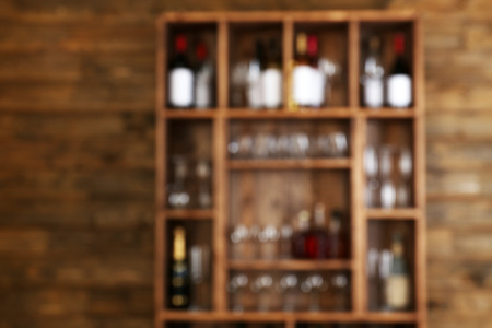 Abstract blurred view of shelving with wine bottles with glasses on wooden wall backgroundの写真素材