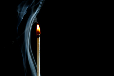 Burning match in smoke on dark background